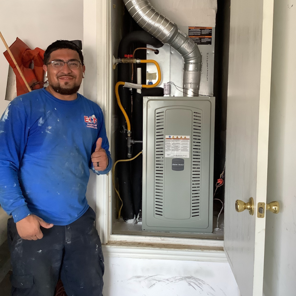 e+m emergency air conditioning technician smiling with a thumbs up next to a repaired furnace in buda home