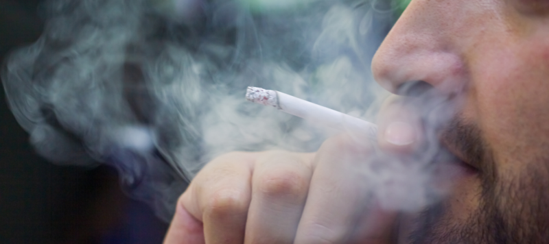 closeup of cigarette being smoked by man with clouds of smoke surrounding the man