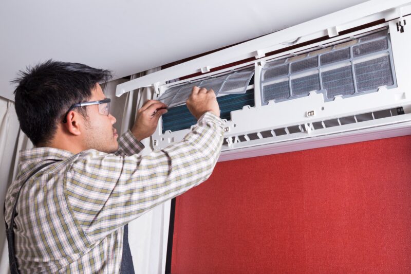 technician repairing ductless ac unit that's posted on red wall