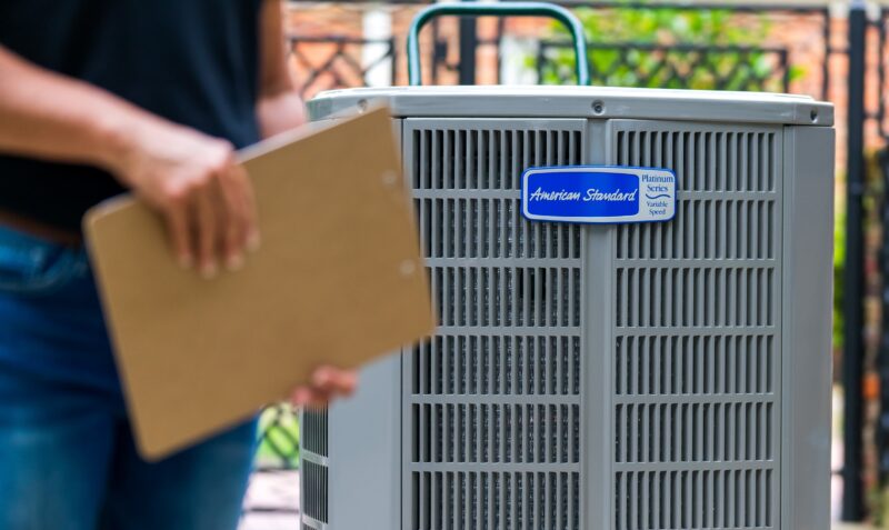 technician holding a clipboard while standing in front of an american standard outdoor hvac unit