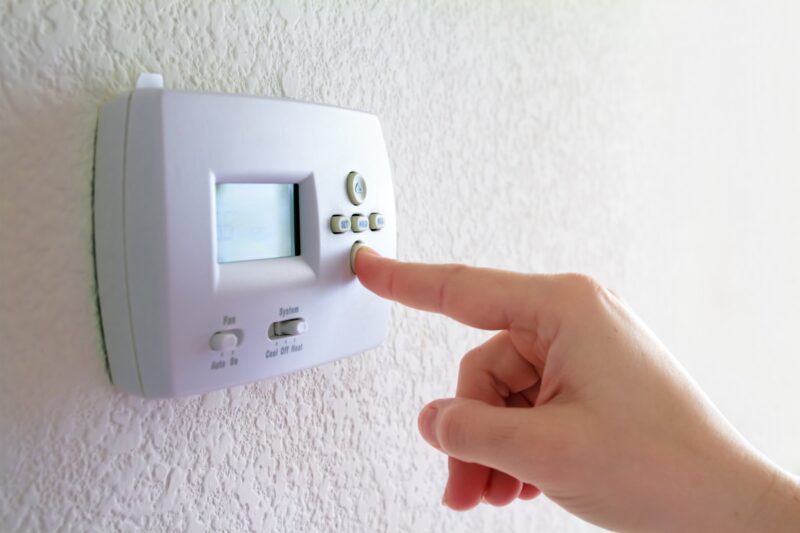 hand adjusting thermostat in their home to increase efficiency